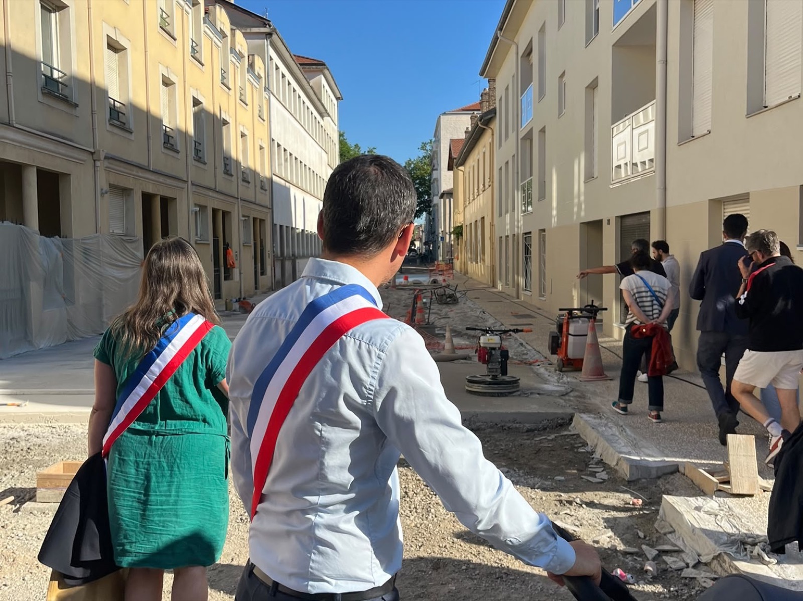 Des élus ceints de leur écharpe tricolore parcourent la rue en chantier devant l'école Louise.